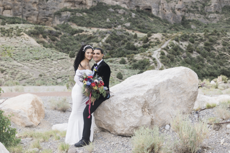 A groom sits on the edge of a large boulder and holds his new wife close on their wedding day at Lee Canyon outside of Las Vegas.