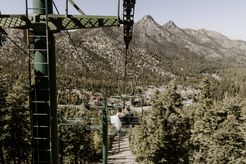 Mountain peaks and pine trees fill the frame as a bride and groom admire the view while riding down the mountain on the ski lift at Lee Canyon outside of Las Vegas on their wedding day.