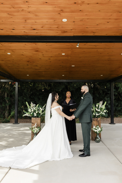 A bride and groom hold hands during their wedding ceremony under the pergola at Lotus House.