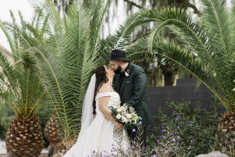 A bride and groom kiss surrounded by palm trees in the garden at Lotus House in Las Vegas.