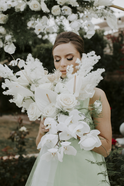A bride dreamily poses with her bouquet of white roses and orchids.