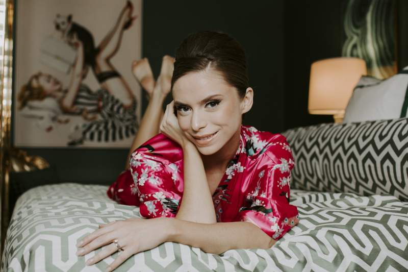 A woman in pink silk floral pajamas lies on a bedspread with a midcentury modern print.