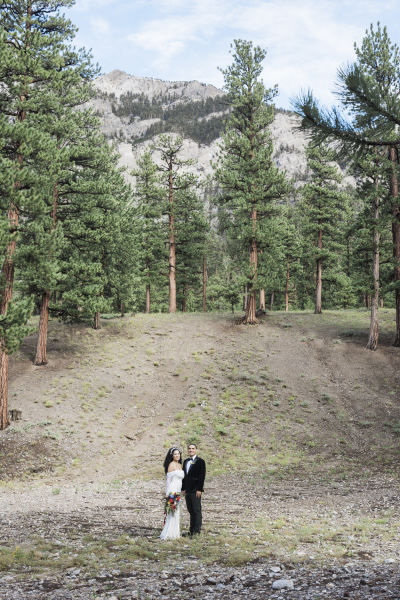 A wide shot of a bride and groom standing at the base of a gentle slope in a clearing in the Spring Mountains outside of Las Vegas.