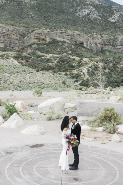 A bride and groom stand in the center of a paved spiral design built into the ground.and bow their foreheads to touch each other as they pose for photos on their wedding day.