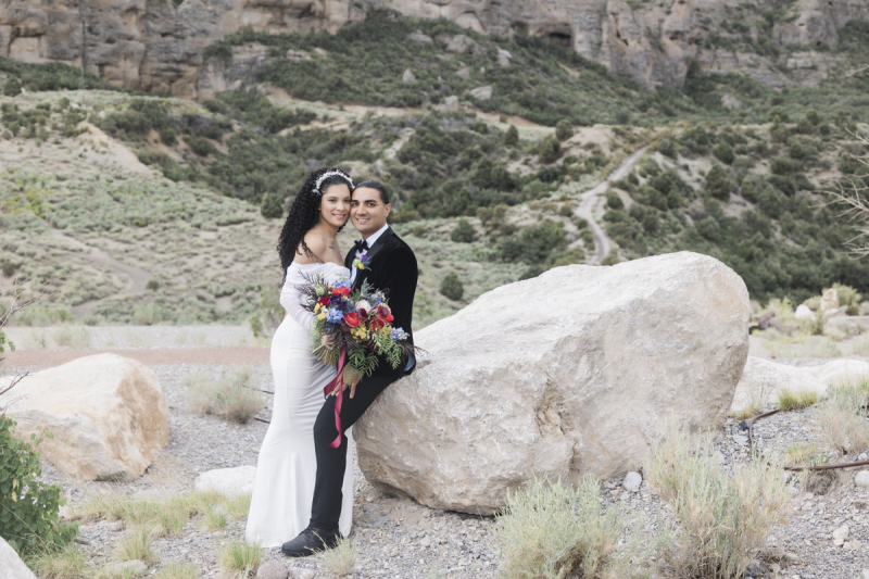 A groom sits on the edge of a large boulder and holds his new wife close on their wedding day in the Spring Mountains range outside of Las Vegas.