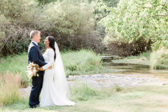 A bride and groom stand in a field near a stream smiling at each other in Black Hills, ND.