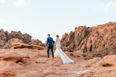 A bride and groom walk up red rocks in the Valley of Fire.