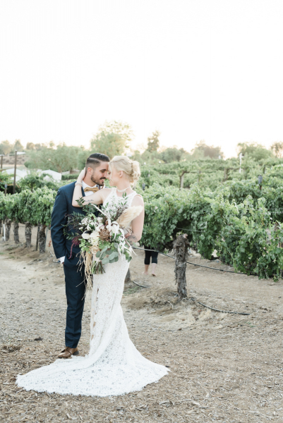 Wedding couple standing in vineyard with foreheads touching.