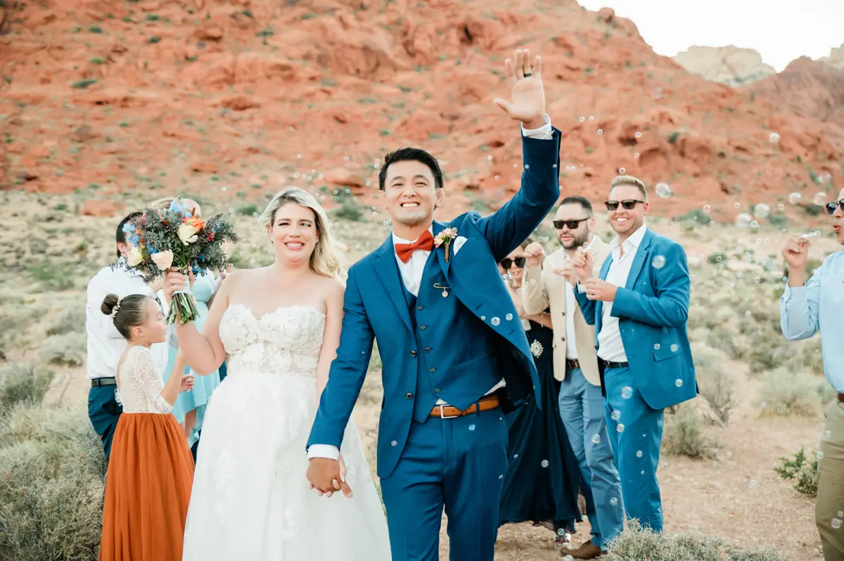 a bride and groom hold hands and walk through bubbles blown by their guests.
