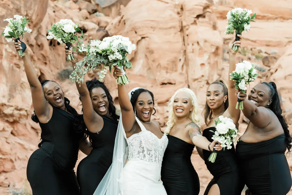 Happy bride and bridesmaids raising their bouquets against red rock formations during a Las Vegas wedding.