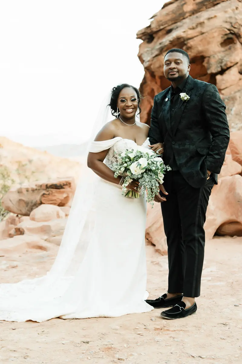 Smiling bride and groom posing against desert red rock formations for their las vegas wedding. A bride and groom sharing a romantic kiss in a desert landscape during their las vegas wedding, with the groom lifting the bride into the air against a sunset sky.