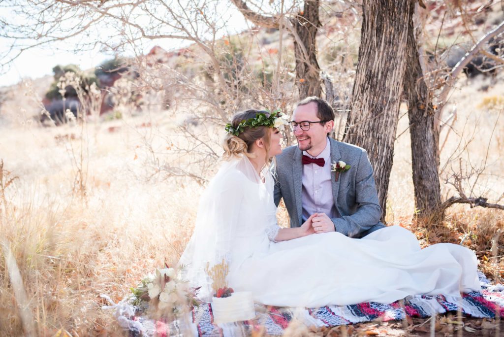 Bride and Groom sit on a plaid cozy blanket during a fall wedding photo shoot.