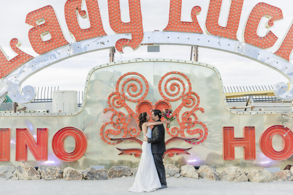 Newlywed couple standing in front of Lady Luck sign at the Neon Museum.
