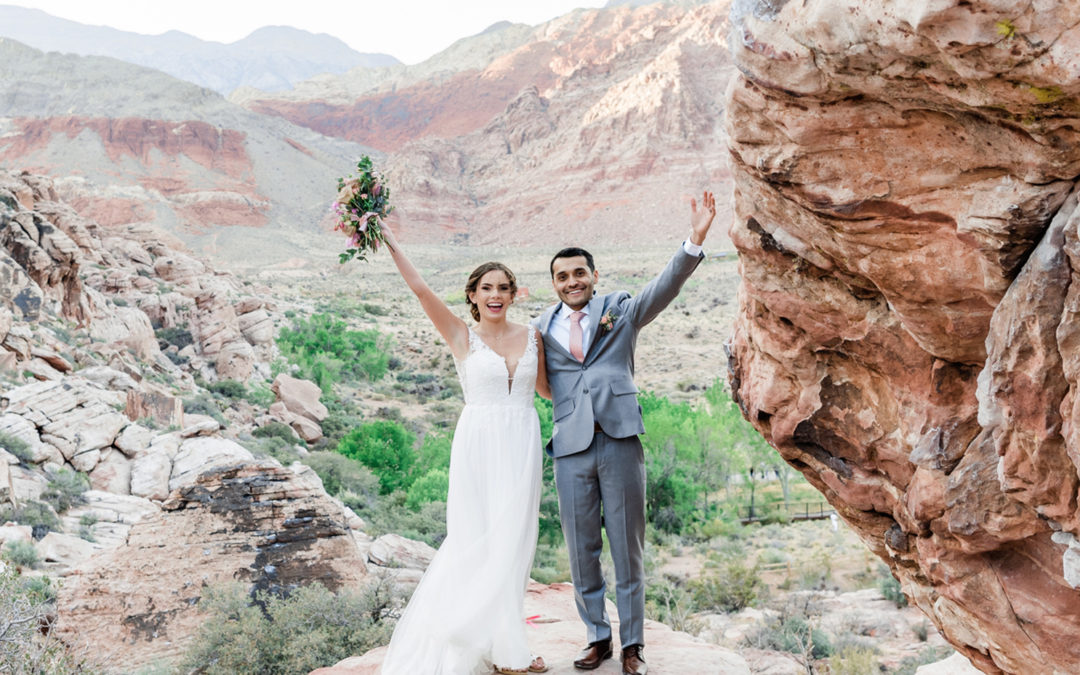 Bride and groom with arms in the air on mountain.