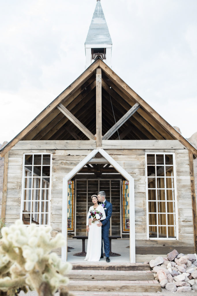 Newlywed couple embracing in front of outdoor chapel