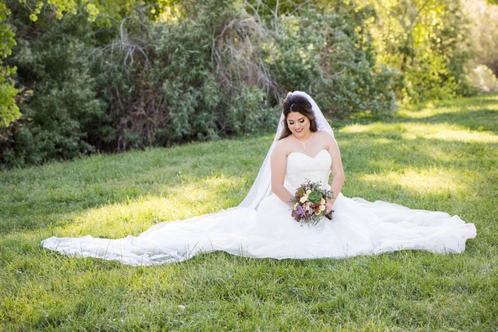 Bride in wedding dress with flowers poses on green lush lawn of park.