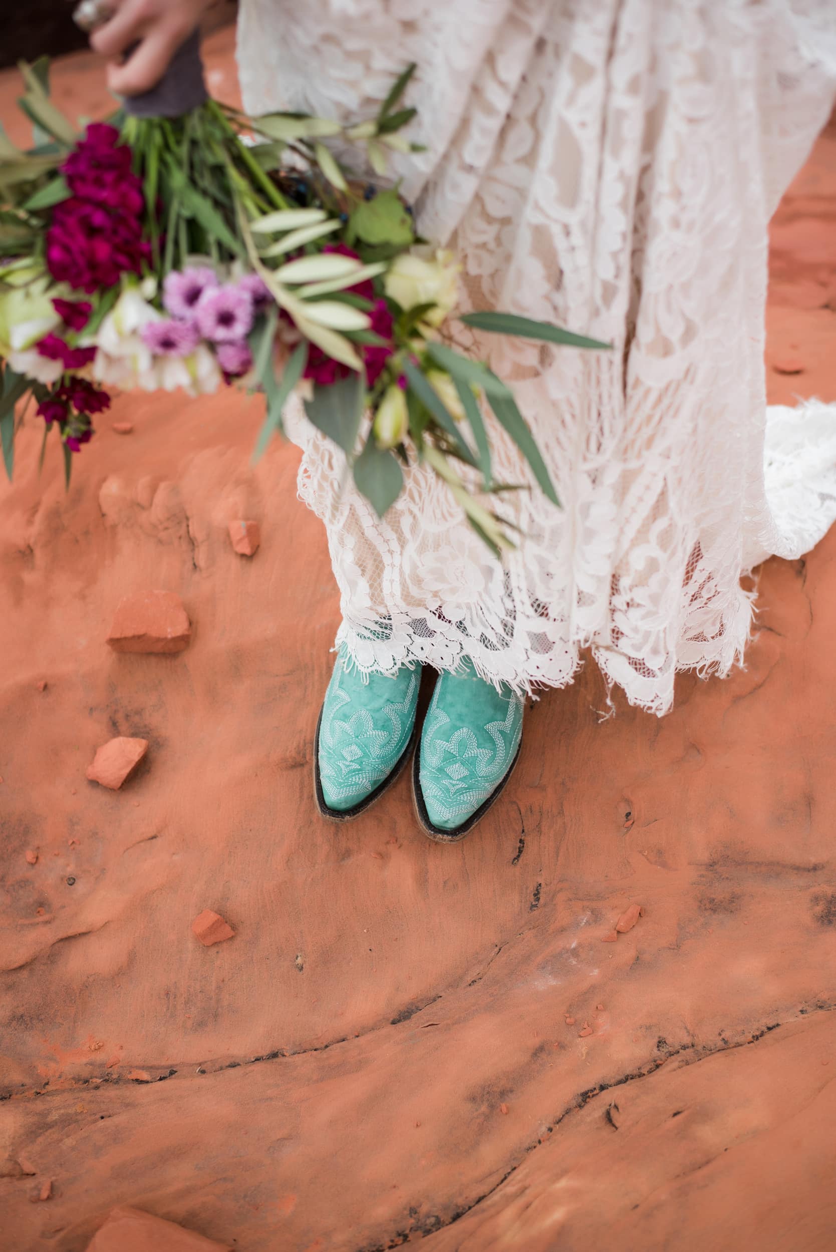 Person in white dress and blue cowboy boots holding a wedding bouquest.
