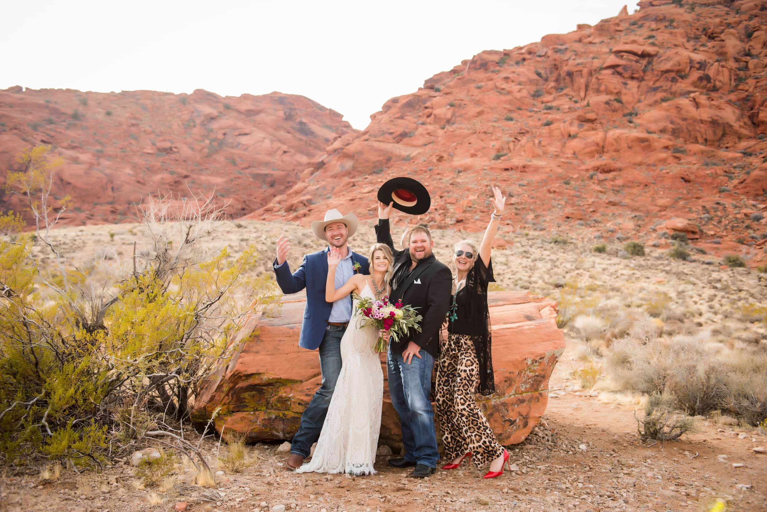 Group of four people in the desert with their arms raised at a western themed wedding