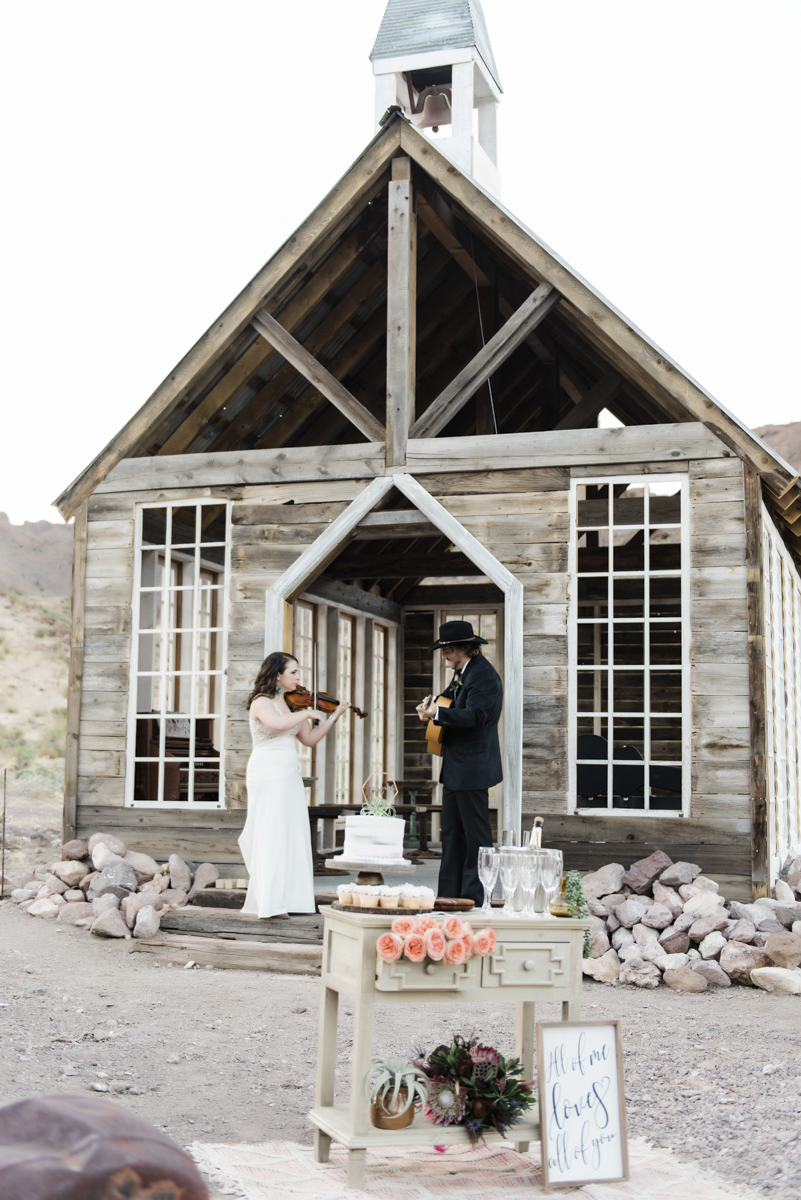 Groom and bride playing musical instruments in front of the the Eldorado Canyon elopement chapel in Las Vegas.
