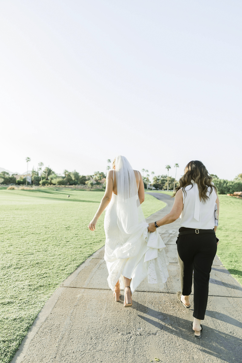 Wedding planner assisting the bride walking in long bridal gown.