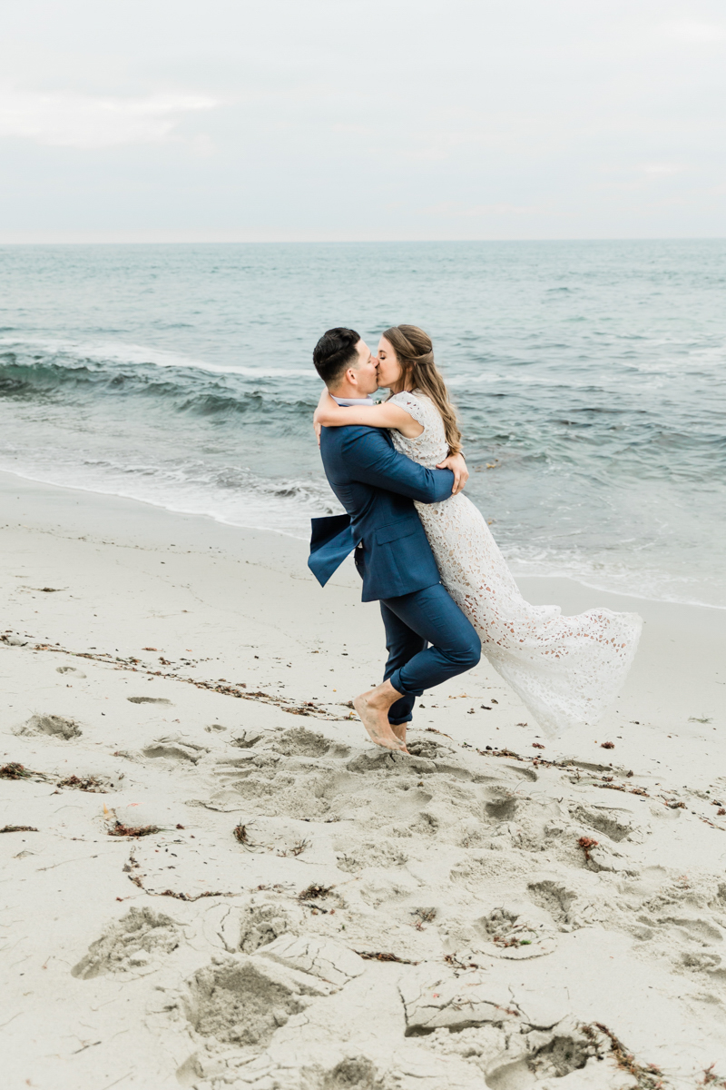 barefoot groom lifting and kissing bride on beach