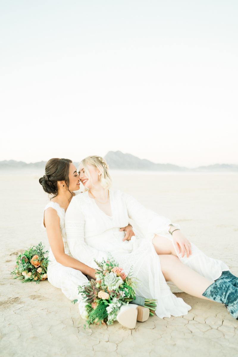 two brides seated on dry lake bed kissing
