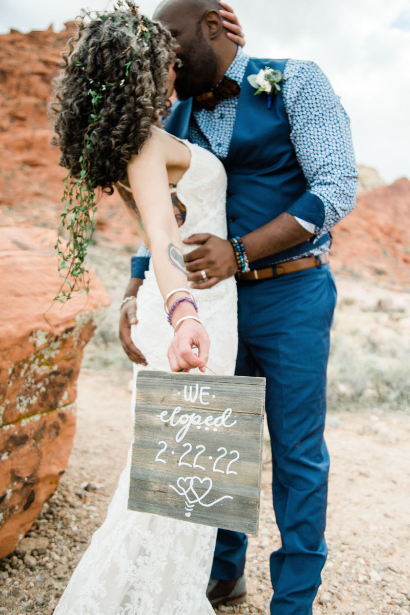 groom kissing bride holding sign with date 2.22.22