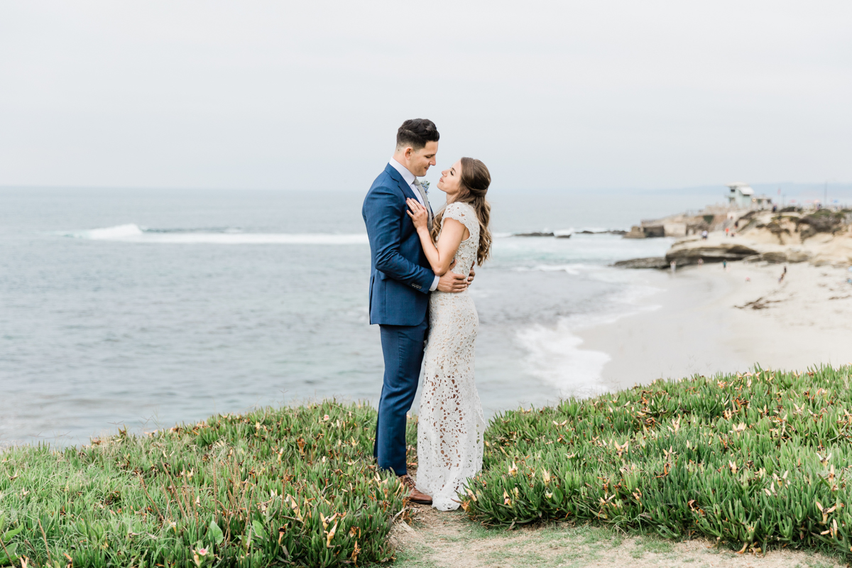 bride and groom standing on hill overlooking ocean in san diego