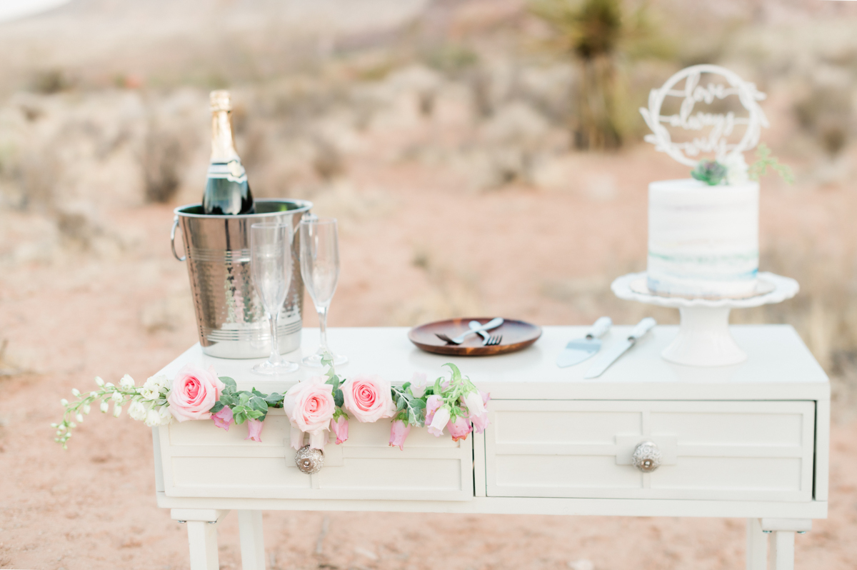 Table set in the desert with champagne and wedding cake.