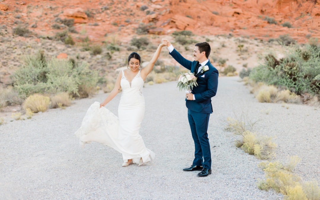 a groom holds a brides hand up in the air as she walks and swishes her dress and laughs.