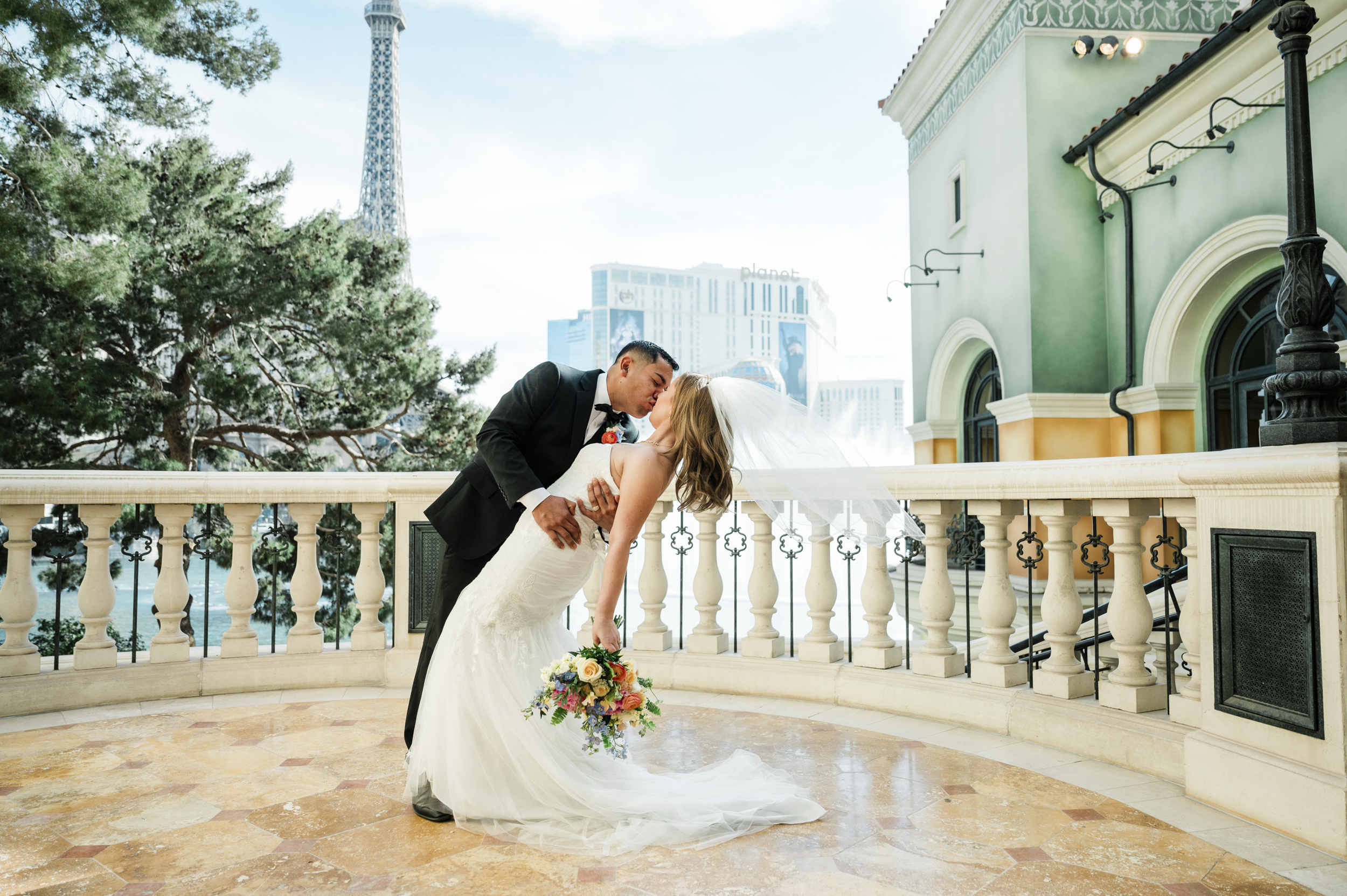 A couple shares a romantic dip and kiss on a balcony overlooking iconic Bellagio fountains.